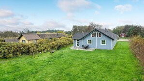 A single-story house with a sloped roof, a small porch with a table and chairs, and a well-maintained lawn. - Beach front home in Hvide Sande with sauna (Hvide Sande)
