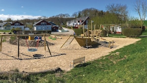 Une aire de jeux avec des balançoires, un toboggan et une structure de jeu en forme de bateau.