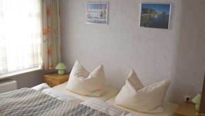 A bedroom with a bed, two pillows, a nightstand, a lamp, a window with curtains, and two framed pictures on the wall.