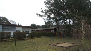 A grassy outdoor area with a playground structure, a wooden bench, and a building with a garage.