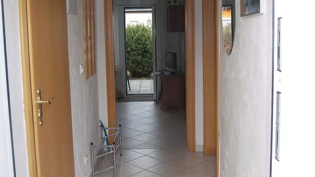 A hallway with a tiled floor, wooden doors, and a view into a room with a tiled floor and a window.