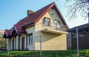 A two-story house with a red roof, a balcony with a metal railing, and a chain-link fence in front. - 2 bedroom lovely home in Mielno (Mielno)