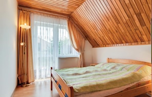 A bedroom with a sloped ceiling, a bed with a colorful blanket, a floor lamp, and sheer curtains. - 2 bedroom lovely home in Mielno (Mielno)