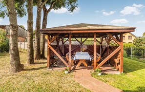 A wooden gazebo with a table and chairs, surrounded by trees and a brick wall. - 2 bedroom lovely home in Mielno (Mielno)