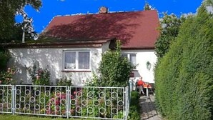 Une maison avec un toit rouge, des murs blancs et une clôture en métal au premier plan.