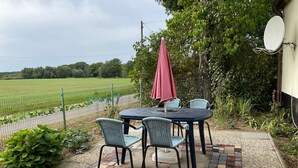 Une terrasse extérieure avec une table et des chaises, un parasol rouge et une vue sur un champ verdoyant.