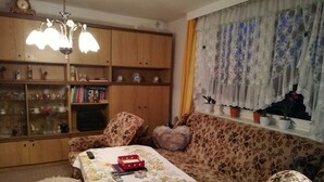 Un salon chaleureux avec un canapé à motifs floraux, un meuble en bois doté de portes en verre et une table recouverte d’une nappe à motifs floraux.