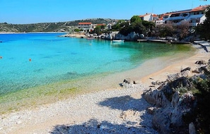 Ein Küstenstrand mit klarem türkisblauem Wasser, felsigem Ufer und Gebäuden mit roten Dächern.