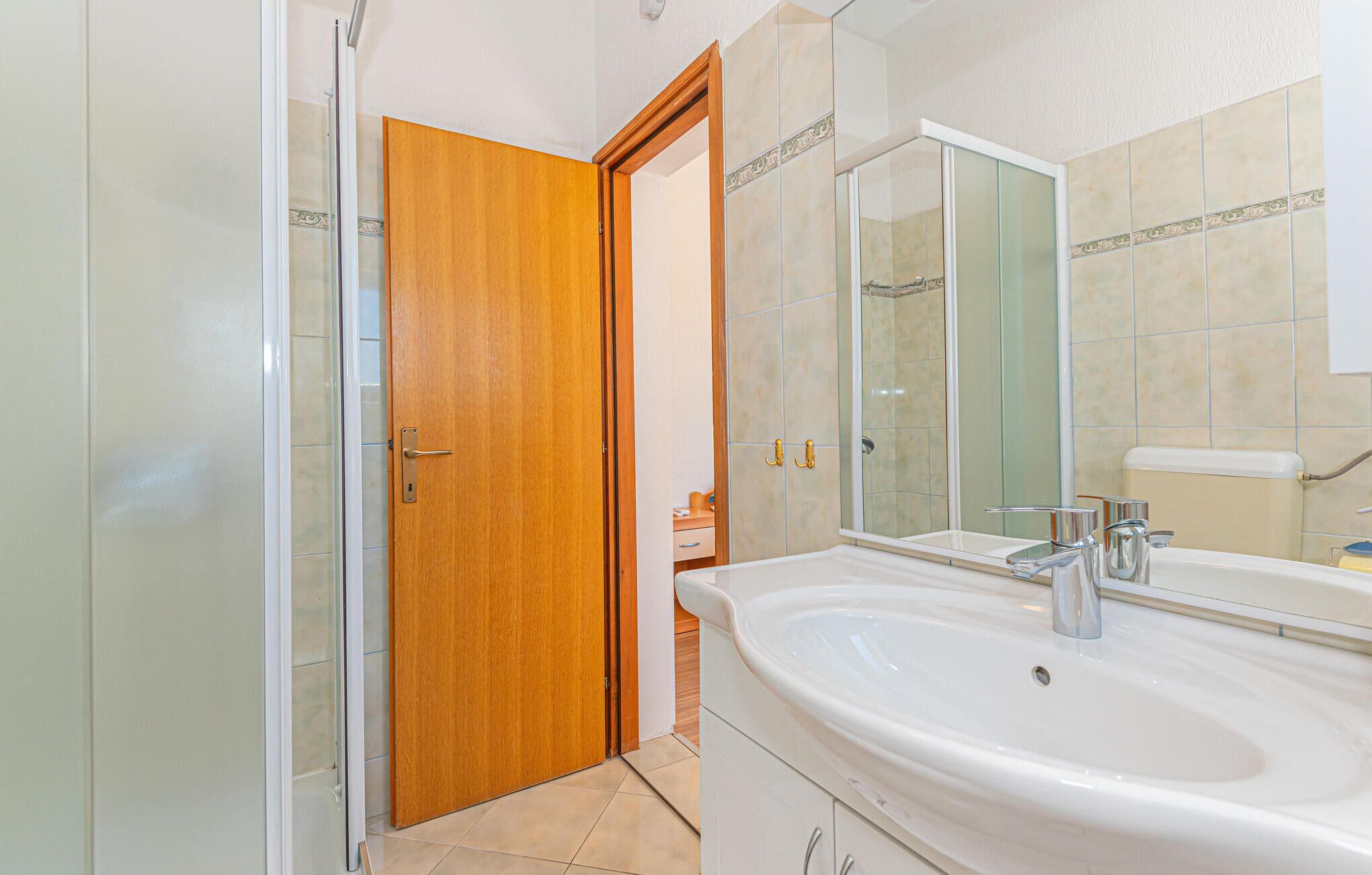 Une salle de bain avec une porte en bois, un grand miroir, un lavabo et un espace douche.