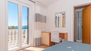 A bedroom with a large bed, a desk, a chair, a small cabinet, a mirror, and a sliding glass door leading to a balcony with a view of the sea. - Gorgeous apartment in Kanica with WiFi (Kanica)