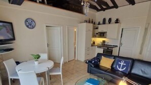 Un espai habitable compacte amb zona de dinar, un sofà amb coixins de temàtica marina, una taula de cafè de vidre i una cuineta.
