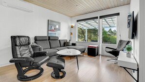 Un salon moderne avec un canapé, deux fauteuils en cuir noir, une petite table ronde et un téléviseur fixé au mur.