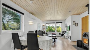 Un salon moderne comprenant un coin repas, de grandes fenêtres, une cheminée et une vue sur la verdure.