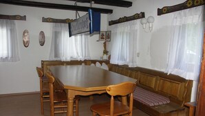 Un espace repas avec une table et des bancs en bois, une enseigne suspendue et une fenêtre avec des rideaux.