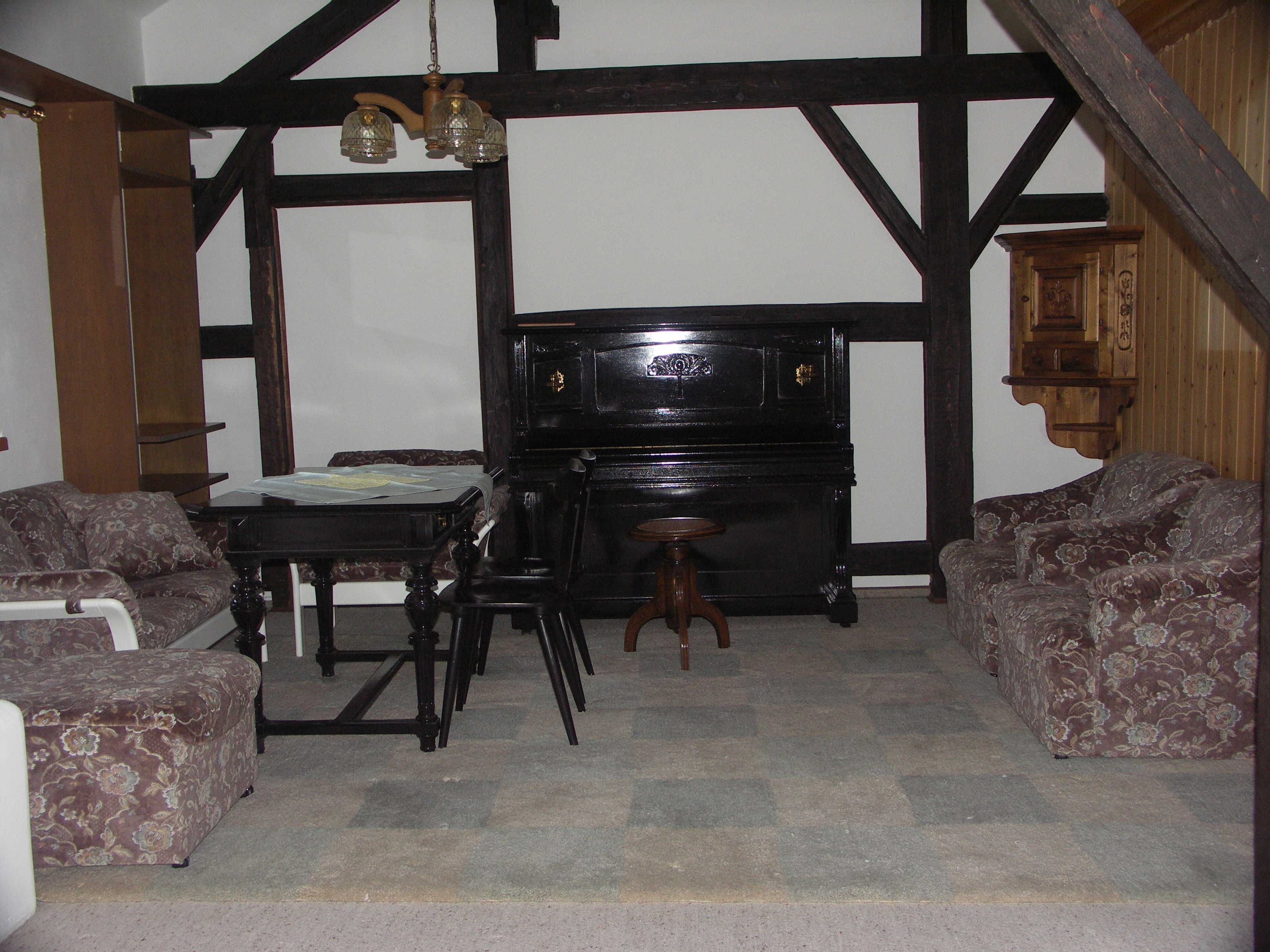 A room with a piano, two patterned sofas, a small table, and a hanging light fixture.