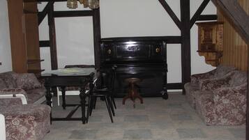 A room with a piano, two patterned sofas, a small table, and a hanging light fixture.