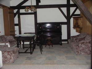 Ein Zimmer mit einem Klavier, zwei gemusterten Sofas, einem kleinen Tisch und einer hängenden Leuchte.