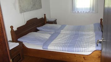 A single bed with a wooden frame, a bedside table, a nightstand, and a window with sheer curtains.