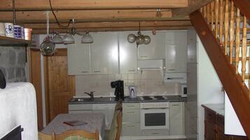 A compact kitchen with wooden beams, a dining table with chairs, and a built-in oven.