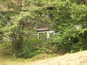 Un bâtiment abandonné envahi par la végétation, une enseigne visible avec du texte, et une structure en bois rustique.