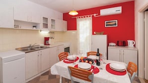 Una cucina compatta con mobili bianchi, un lavello e un'area da pranzo per quattro persone, con tavolo, sedie e tovaglia rossa.