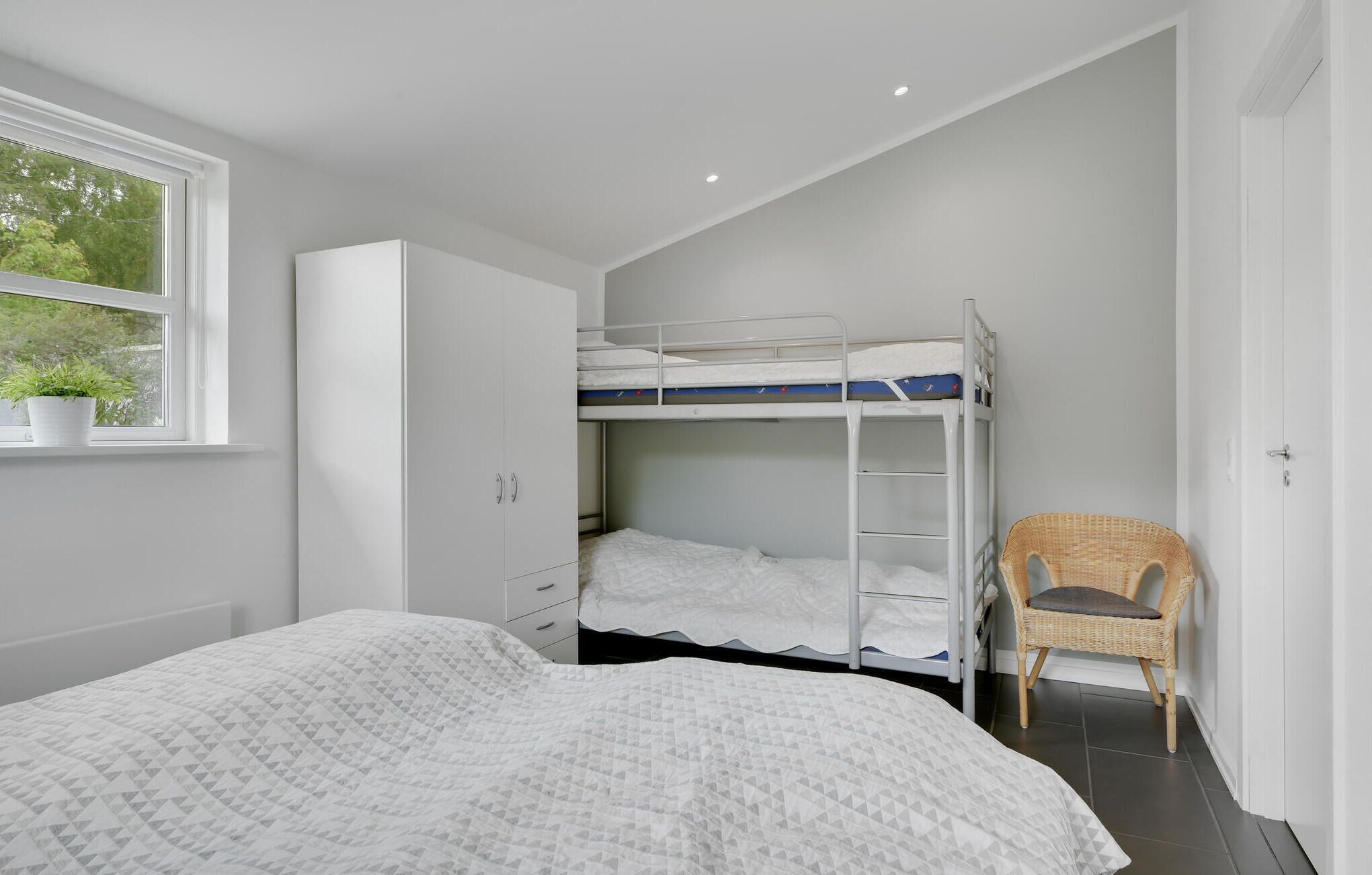 A bedroom with a bunk bed, a single bed, a wardrobe, and a chair.
