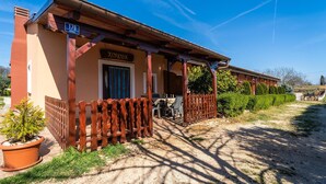 A building with a wooden porch, a sign reading "KONOVA", and a dirt path leading to it.