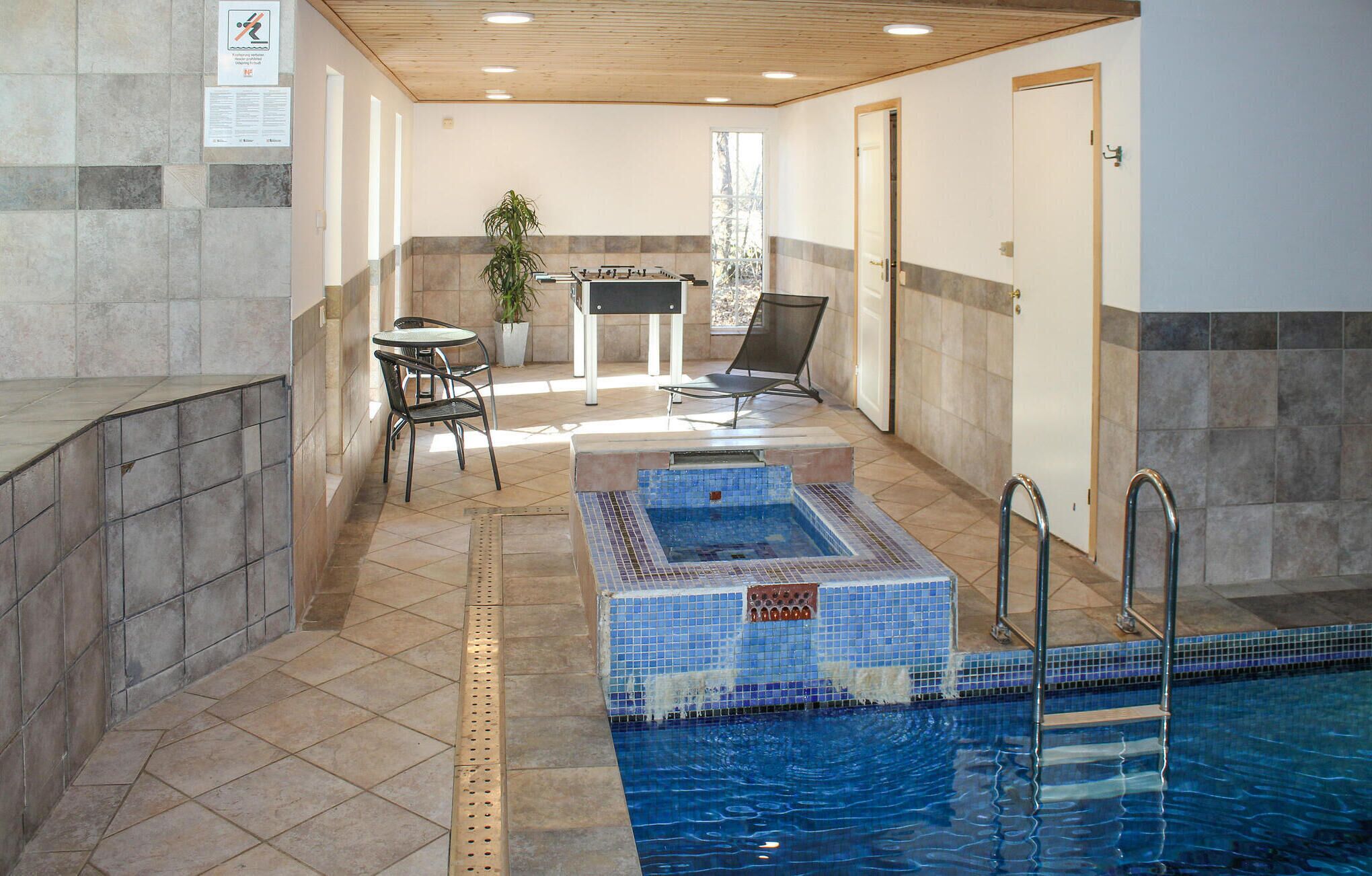 Una piscina interior con suelo de baldosas, una mesa de billar pequeña y un área de descanso con sillas y una mesa.