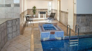Une piscine intérieure avec un sol carrelé, une petite table de billard et un espace détente avec des chaises et une table.