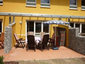 An outdoor patio with a table and chairs, a wicker chair, a stone wall, and a window.