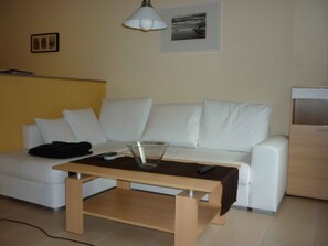 A modern living room with a white sofa, a glass coffee table, and a remote control on the table.