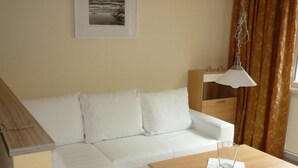A white sofa, a wooden table, a framed picture on the wall, and a window with curtains.