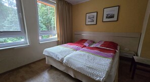 A bedroom with a bed, two framed pictures on the wall, and a window with curtains.
