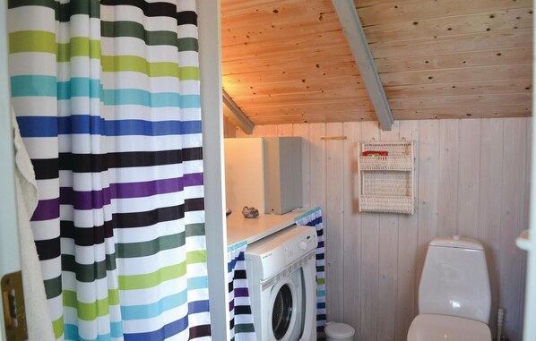 A compact bathroom with a washing machine, a toilet, and a shelf with baskets. - Stunning home in Knebel (Knebel)
