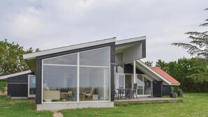 A modern house with a large glass front, a sloped roof, and a patio area with outdoor furniture. - Stunning home in Knebel (Knebel)