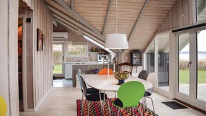 A modern kitchen with wooden beams, a dining area with colorful chairs, and a large window offering a view of the outdoors. - Stunning home in Knebel (Knebel)