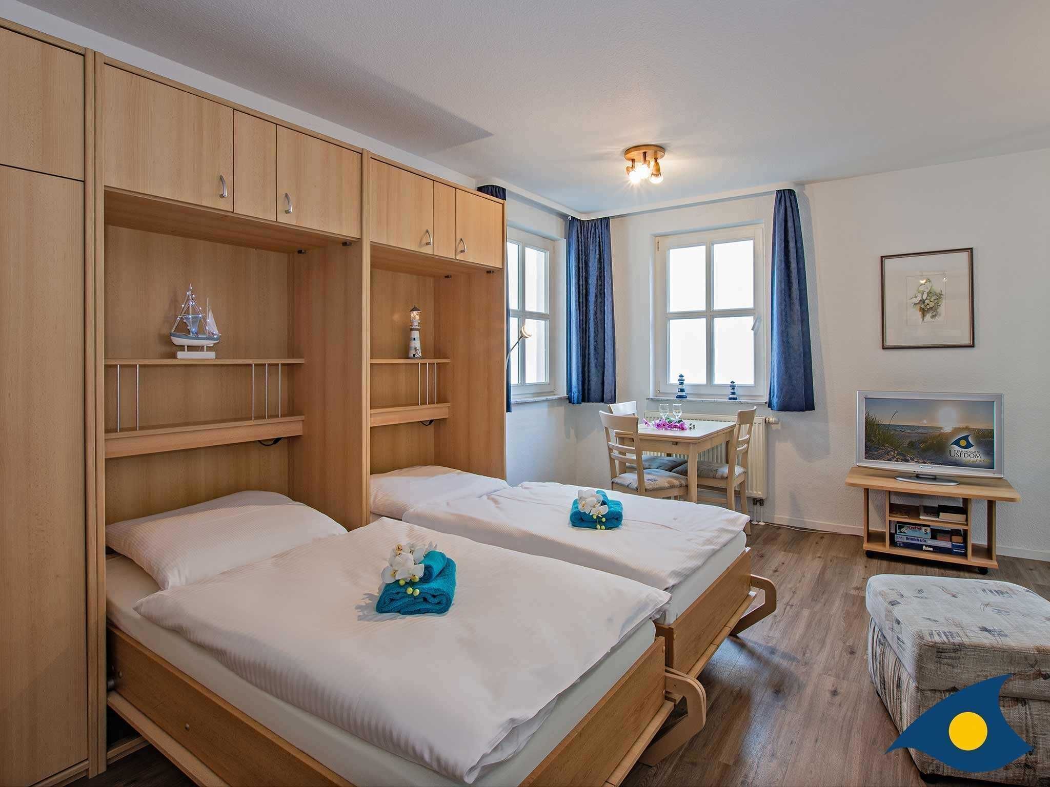 A room with two beds, a desk, a television, and a window with curtains.