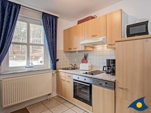A compact kitchen with wooden cabinets, a built-in oven, a dishwasher, and a microwave. - Villa Margot, Whg. 06 - VM 06 (Heringsdorf)