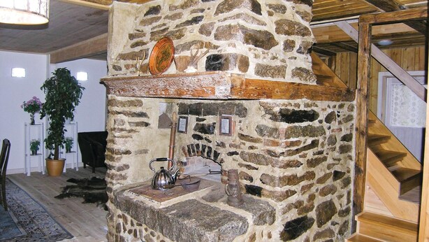 Ein Steinkamin mit einer Metallkessel und einem Teller darauf, umgeben von Holzbalken und einer Treppe.