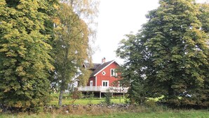 Ein rotes Haus mit weißer Veranda, umgeben von Bäumen und einer Steinmauer.