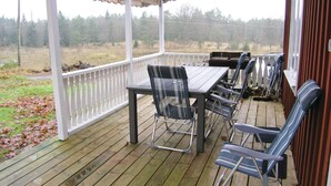 Eine überdachte Terrasse im Freien mit Tisch und Stühlen, mit Blick auf eine bewaldete Landschaft.
