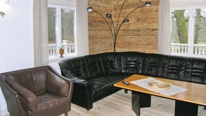Ein Wohnzimmer mit schwarzem Ledersofa, einem Holztisch, einem braunen Ledersessel und einer hohen Stehlampe.