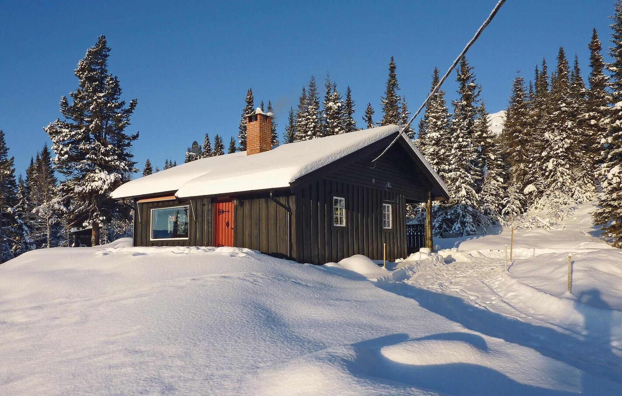 A cabin with a snow-covered roof, a red door, and a window overlooking a snowy landscape.
