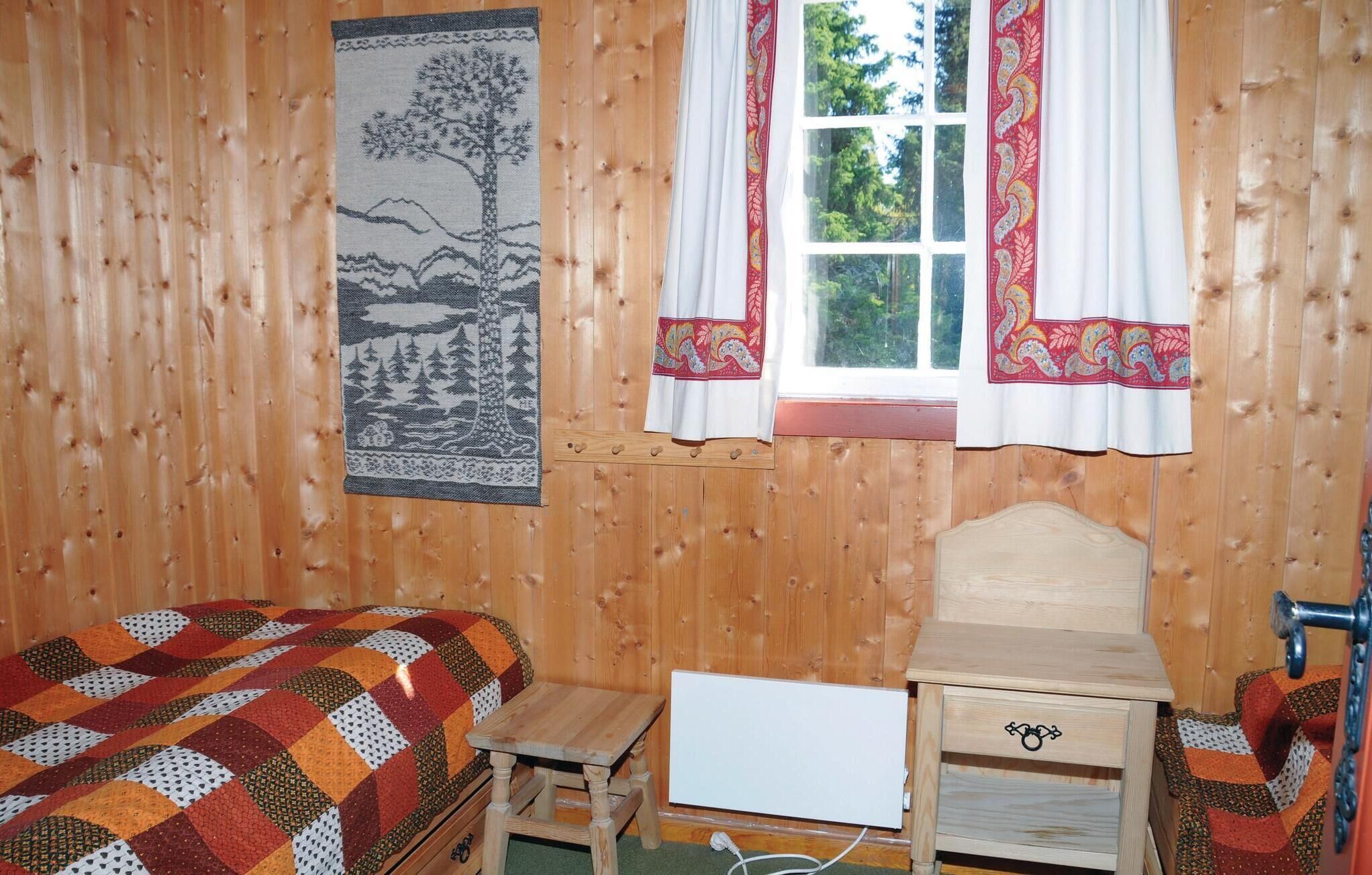 A wooden room with a bed, a small table, a desk, and a window with curtains.