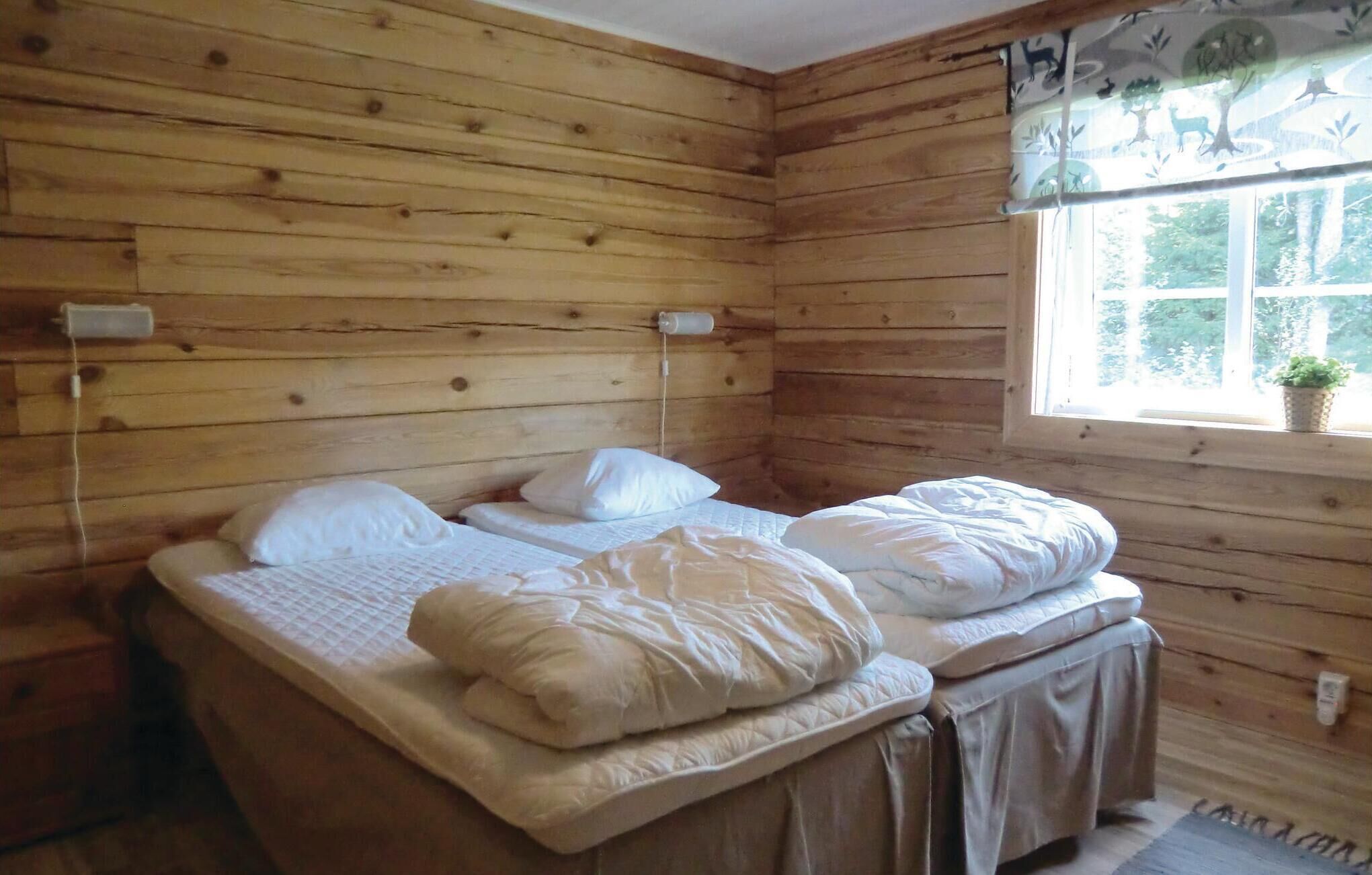A wooden cabin room with two beds, a window with a view of trees, and a small plant on the windowsill.