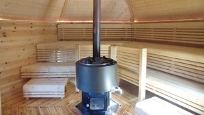 Una sauna de madera con calentador central, bancos y techo inclinado.