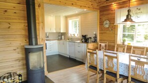 Interior acogedor de una cabaña con estufa de leña, un comedor con sillas de madera y una cocina con armarios blancos.