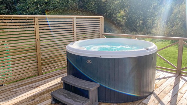 Un jacuzzi en una terraza de madera con vistas a un área boscosa.
