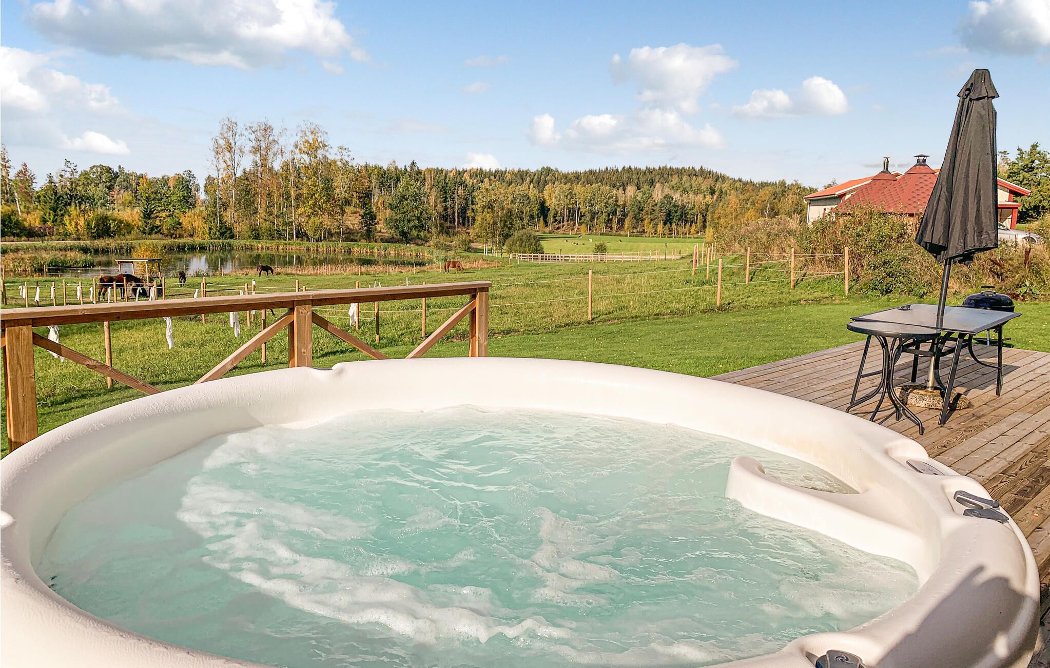 Un bain à remous sur une terrasse en bois, avec vue sur un champ verdoyant et des arbres en arrière-plan.