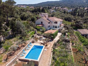 Uma casa de dois andares com piscina, cercada por árvores e colinas.